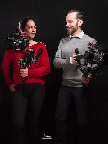 Portrait de deux vidéastes professionnels en tenue noire et rouge tenant leur caméra – RNT Motion, spécialistes du mariage, événementiel et documentaire